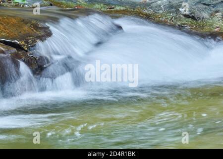 Über die Steine fließt ein klarer Strom, der einen kleinen Wasserfall bildet, Wasserstrahlen sind in Bewegung verschwommen Stockfoto