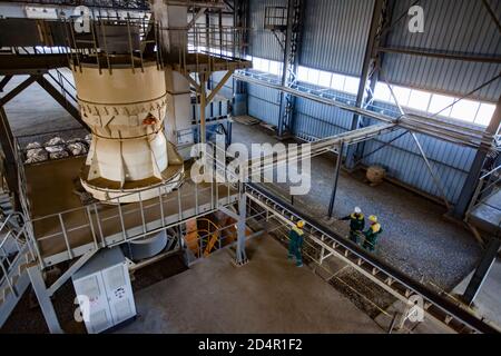 Region Aktobi/Kasachstan - Mai 04 2019: Phosphatdüngeanlage. Maschine für Pellets Produktion. Transporteur und drei Arbeiter. Stockfoto