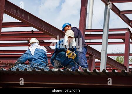 Shymkent, Kasachstan. Industriegebäude der chemischen pharmazeutischen Fabrik Santo. Zwei Arbeiter und Schweißer auf dem Dach machen Stahlverstärkung arbeiten. Stockfoto