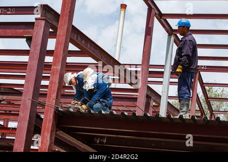 Schymkent/Kasachstan - April 27 2012: Bau eines neuen Industriegebäudes. Zwei Arbeiter und Schweißer auf dem Dach macht Verstärkung Stahlarbeiten. Stockfoto