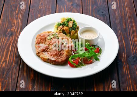 Gebratenes Schweinekotelett mit Kartoffelpüree und Boletus edulis Soße serviert mit frischer Tomatenkirsche und Rucola Stockfoto