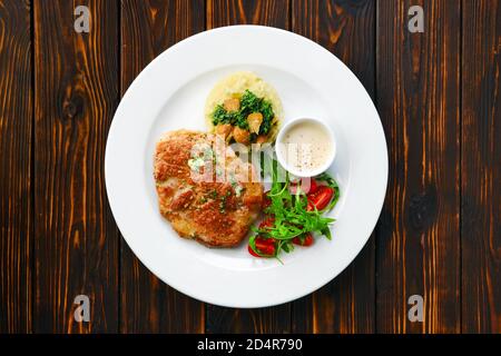Draufsicht auf gebratenes Schweinekotelett mit Kartoffelpüree Und Boletus edulis Soße serviert mit frischen Tomatenkirschen und Rucola Stockfoto