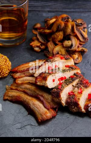 Gebratenes Fleisch serviert mit gebratenen Pilzen und einer Scheibe Speck, Senf und einem Glas Bourbon Stockfoto