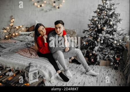 Fröhliches Paar im Winter Pullover verbringen Winterurlaub zu Hause Liegen auf gemütlichem Bett neben einem Weihnachtsbaum Stockfoto