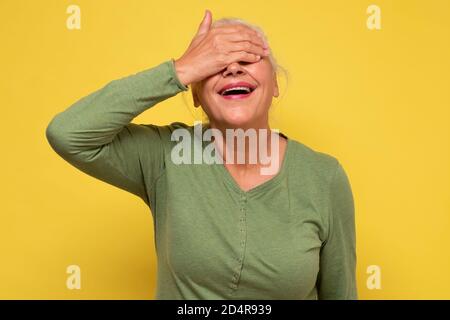 Ältere schöne Frau lächelnd deckende Augen für Überraschung Stockfoto