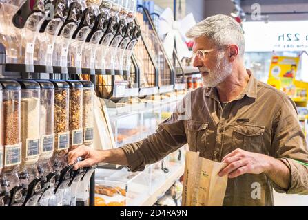 Mann nimmt trockene Früchte aus Spender in Bio-Supermarkt. Stockfoto