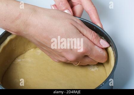 Eine Frau legt den gerollten Teig in eine Backform. Nahaufnahme. Levington Kuchen, Stufen der Vorbereitung. Stockfoto