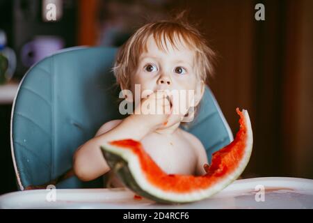 Glücklich Kleinkind Junge essen Wassermelone in seinem Hochstuhl Stockfoto