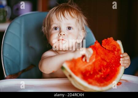 Glücklich Kleinkind Junge essen Wassermelone in seinem Hochstuhl Stockfoto