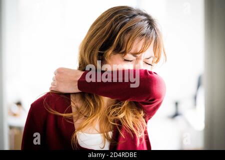 Frau bedeckte ihr Gesicht mit seinem Arm zu niesen. Stockfoto