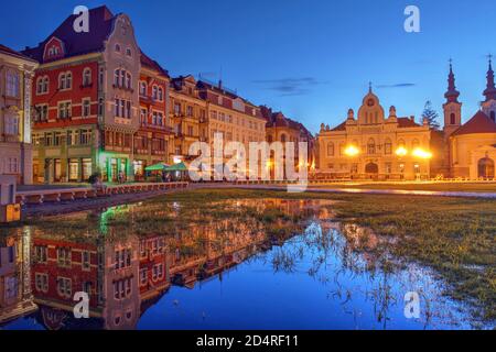 Nachtszene auf dem Unirii-Platz (Union Square), Timisoara, Rumänien mit einer Reihe von historischen Häusern, die sich in einem temporären Pool spiegeln Stockfoto