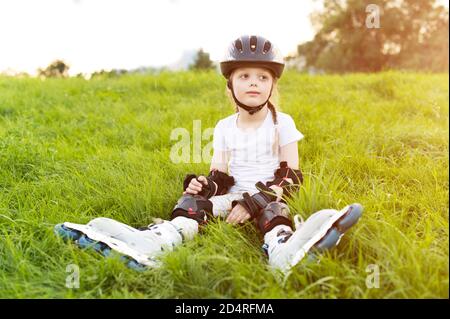 Kleines hübsches Mädchen auf Rollschuhe im Helm in einem Park. Junge glückliche Skater Stockfoto