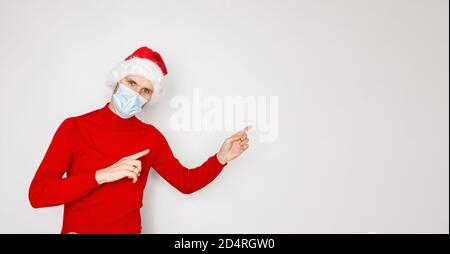 Weihnachten während der Pandemie des COVID-19 Coronavirus-Konzepts. Schöner Mann trägt Einweg-Gesichtsmaske und Santa Hut. Männliche Modell trägt roten Pullover Stockfoto