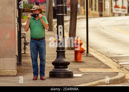 Ellicott City, MD, USA 10/07/2020: Ein Kaukasier mittleren Alters mit Akubra-Hut, Jeans und Cowboystiefeln aus Leder legt sich vor cro eine Gesichtsmaske an Stockfoto