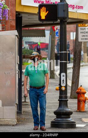 Ellicott City, MD, USA 10/07/2020: Ein Kaukasier mittleren Alters mit Akubra-Hut, Jeans und Cowboystiefeln aus Leder wartet an der Ampel. Er ist es Stockfoto