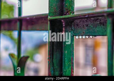 Wassertropfen hängen nach einem Gewitter am Nachmittag während der Monsunsaison in Indien prekärisch an einem Metalltor. Stockfoto