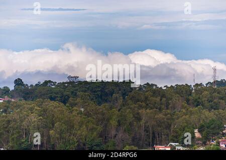 Dicke Monsunwolken Rollen über dem Kamm eines Berges, an einem teilweise sonnigen Oktobertag in Shillong, Meghalaya, Indien. Stockfoto