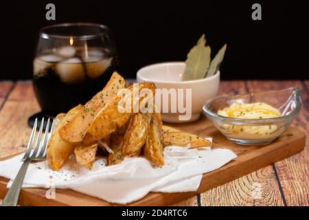 Rustikale oder Landhausstil Pommes mit Kräutern in einer Keramik Schüssel auf einem Holzbrett mit Grillsoße und Mayonnaise Mit Kräutern auf Holztisch Stockfoto