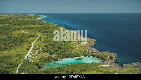 Luftaufnahme des türkisfarbenen Salzwassersees bei grünen tropischen Bäumen. Gebäude und Straße im grünen Tal der Sumba Insel, Indonesien. Erstaunliche Asien Seeslandschaft der Meeresbucht bewundern Felsküste bei Drohne erschossen Stockfoto