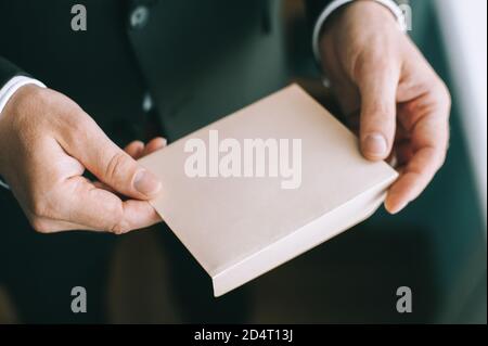 Nahaufnahme der Hände eines erwachsenen ernsthaften Mannes, der einen weißen Umschlag ohne Inschriften hält. Stockfoto