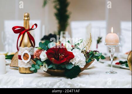 Nahaufnahme eines Blumenarrangements in Rottönen in einem Goldständer steht auf einem Tisch. Stockfoto