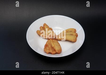 Drei gebratene Bananen werden auf einem weißen Teller serviert. Diese Snacks sind in Indonesien, Singapur und Malaysia zu finden. Stockfoto