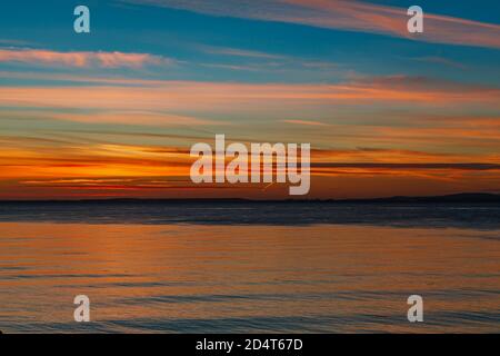 Die Sonne geht über den walisischen Hügeln unter Ein ruhiger Abend am Clevedon Beach und Beleuchtung der Horizont mit Multicoloren Stockfoto