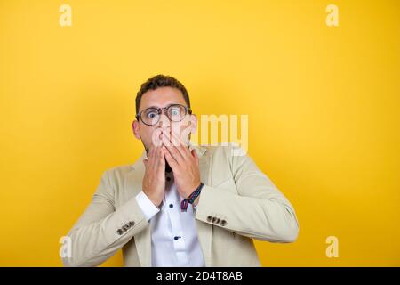 Junge gut aussehende Geschäftsmann tragen Anzug über isoliert gelben Hintergrund mit Ihre Hände über ihrem Mund und überraschten Stockfoto