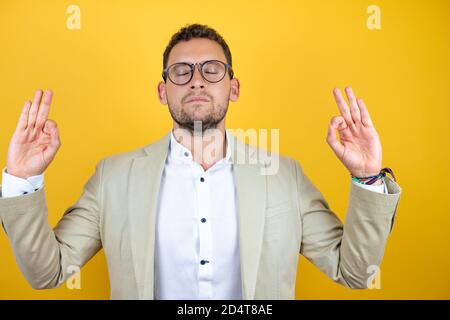Junge gut aussehende Geschäftsmann tragen Anzug über isolierten gelben Hintergrund entspannen und lächeln mit geschlossenen Augen dabei Meditation Geste mit Fingern. Yoga Stockfoto