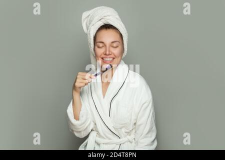 Hübsche junge Frau im weißen Bademantel mit Zahnbürste mit Zahnpasta Stockfoto