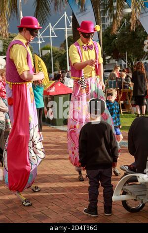 Zwei Stelzenläufer in bunten Clownkostümen unterhalten Kinder. Tauranga, Neuseeland, 10/14/2014 Stockfoto