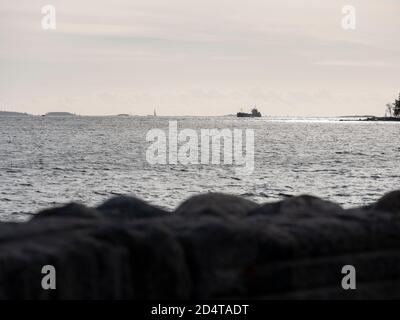 Helsinki/Finnland - 10. OKTOBER 2020: Eine Silhouette eines kleinen Frachtschiffes, das den sonnigen Horizont überquert. Stockfoto