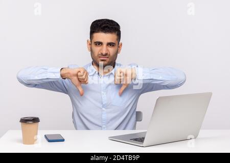 Nicht Gefallen! Unzufriedener Geschäftsmann sitzt Büro Arbeitsplatz zeigt Daumen nach unten Geste, zum Ausdruck bringen Missbilligung, schlechtes Feedback, negative Service-Bewertung. ich Stockfoto