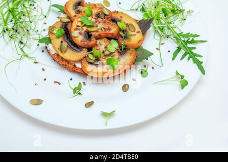 Sandwich mit gebratenen Pilzen, Basilikum, Kürbiskernen und Microgreens – Rettich und Zwiebelsprossen, serviert auf weißem Teller Stockfoto