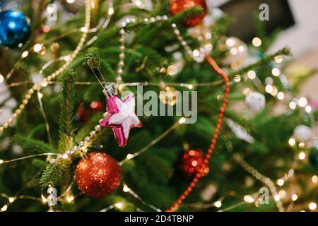 Nahaufnahme eines rosa Weihnachtsbaum-Spielzeugs in Form eines Sterns auf den Ästen eines Weihnachtsbaums. Stockfoto
