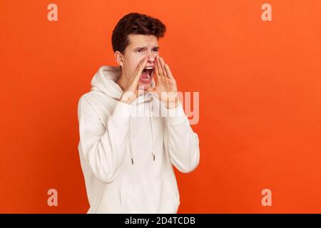 Profilportrait eines hysterischen jungen Mannes, der laut in Panik schreit, die Hände in der Nähe seines Mundes hält, protestiert ein Teenager. Innenaufnahme des Studios isoliert auf Orang Stockfoto