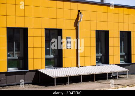 Fassade des Geschäftsgebäudes mit großen Fenstern aus der Nähe. Industriegebäude mit Abfluss und Keller. Die Wand wurde durch moderne gelbe Fliesen restauriert. Heller Laden. Vi Stockfoto