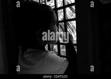Eine Nahaufnahme eines indischen Mädchens, das in monochromen Fotos vor dem Fenster vor der Natur guckt, Kalaburagi, Karnataka/Indien-Oktober 09 2020 Stockfoto