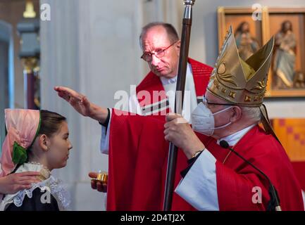 Crostwitz, Deutschland. Oktober 2020. Bischof Konrad Zdarsa (r) schenkt das Sakrament der Firmung unter den Bedingungen der Korona. In der Kirche Crostwitz erhalten etwa 40 Jugendliche eine Bestätigung. Einige Frauen tragen traditionell das sorbische Kostüm. In der katholischen Kirche ist die Firmung eines der Sakramente nach der Taufe und der ersten Kommunion. Quelle: Matthias Rietschel/dpa-Zentralbild/ZB/dpa/Alamy Live News Stockfoto