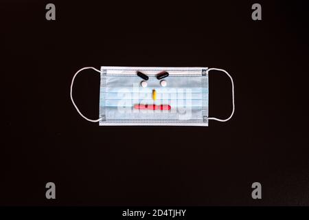 Medizinische Maske mit Pillen auf schwarzem Hintergrund. Lächeln Sie von der Maske und Pillen. Draufsicht. Stockfoto