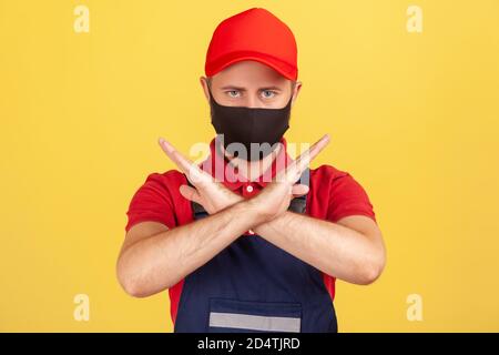 Serious Handwerker in Overalls und Schutzmaske gestikulierenden Stopp mit gekreuzten Händen, Verbot der Arbeit in Quarantäne, professionelle Service-Industrie. Stockfoto