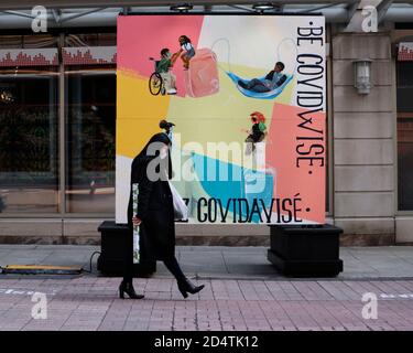 Ottawa, Kanada. Oktober 2020. Frau mit Maske, die an dem neuen 'Be CovidWise'-Poster auf der Sparks Street vorbei geht Stockfoto