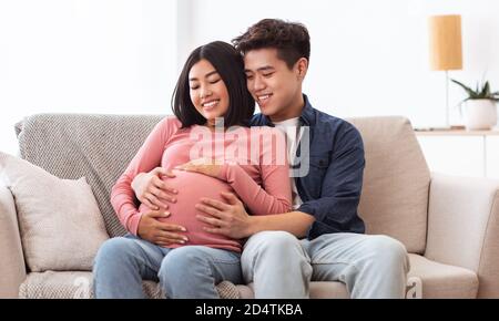 Glücklich Asiatisch Ehemann Umarmt Schwanger Ehefrau Sitzend Zusammen Bei Hause Stockfoto