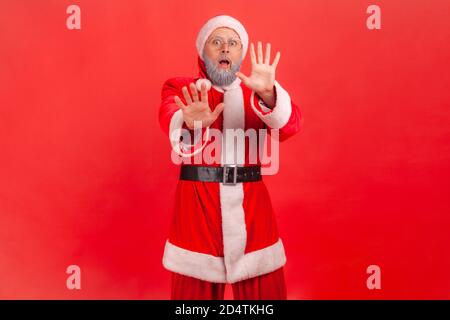 Porträt eines besorgten erschrockenen Mannes im weihnachtsmann Kostüm und Brillen aufsteigende Hände zeigen Stop-Geste, Angst vor Feiertagen, Phobie. Studio im Innenbereich Stockfoto