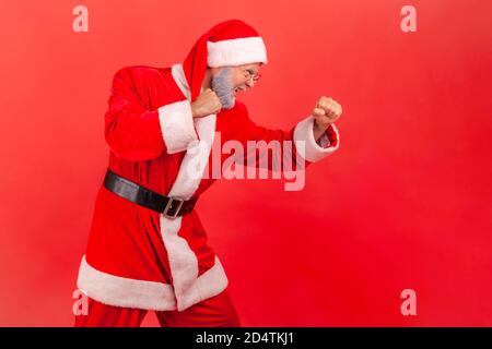 Seitenansicht Porträt von aggressiven zielstrebigen grauen bärtigen Mann hält die Fäuste, kämpfen mit Konkurrenten, vorgeben, weihnachtsmann zu sein, Kampfgeist o Stockfoto