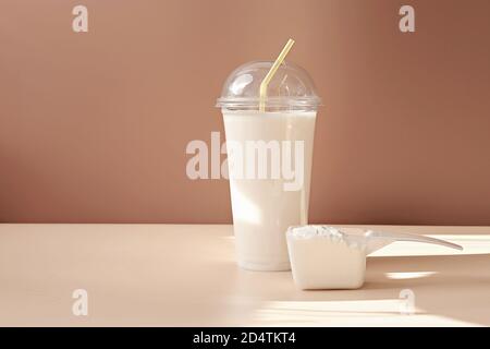 Vorderansicht von Molkenproteincocktail in einer Einweg-Tasse und Schaufel von Kollagenpulver auf einem beigen Hintergrund. Kollagen Peptide trinken für Gelenke und Schönheit. Protein Shake in Take Away Tasse. Stockfoto