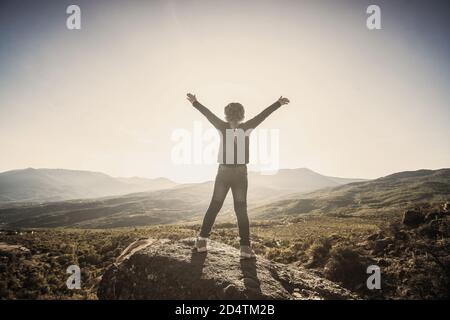 Kleines Mädchen auf einem Felsen in den Bergen. Das Kind streckte seine Arme zur Sonne. Hochwertige Fotos Stockfoto