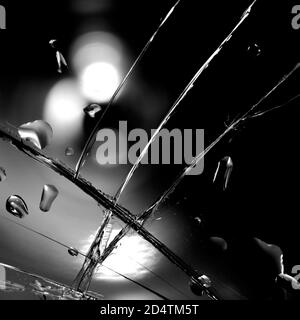 Gebrochener Glashintergrund in schwarz. Schwarzer minimalistischer Hintergrund mit Rissen auf dem Glas mit Wassertropfen. Stockfoto