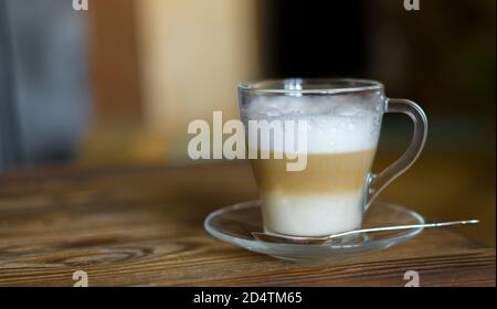 Latte auf rustikalem Holztisch. Glas Tasse auf Glas Untertasse mit einem Löffel Kaffee Latte. Geringe Schärfentiefe. Stockfoto