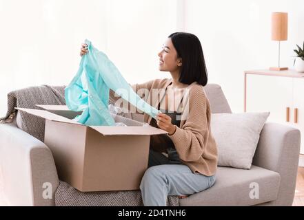 Glückliche asiatische Käufer Auspacken Kleidung nach Online-Shopping Stockfoto